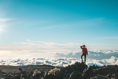 Man standing on rock looking at mountain against sky