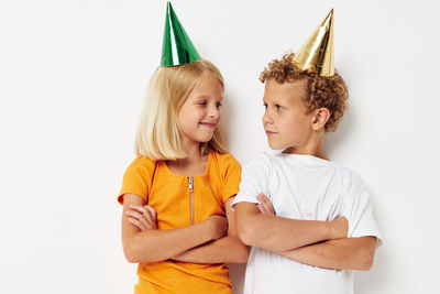 Happy girl and boy wearing party hat standing against white background