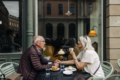 Senior man holding hand of woman while sitting together at sidewalk cafe