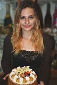 Portrait of smiling young woman holding cake at home