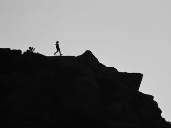 Low angle view of silhouette man standing on rock against sky
