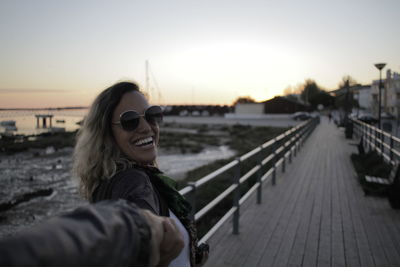 Young woman on pier at beach against sky during sunset