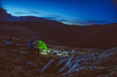Person camping on mountain against blue sky at dusk