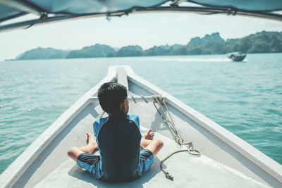 Rear view of man sitting on boat sailing in sea