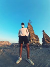 Rear view of man standing on rock against clear sky