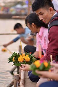 Young couple holding flowers with incense by river