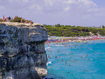 Group of people on rock by sea against sky