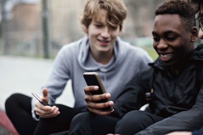 Phone addictive happy friends sitting on sidewalk in city