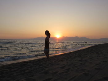 Silhouette of woman standing on shore during sunset