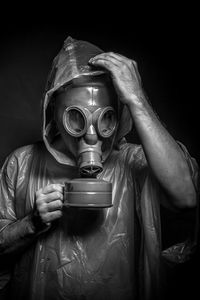 Man in raincoat wearing gas mask against black background
