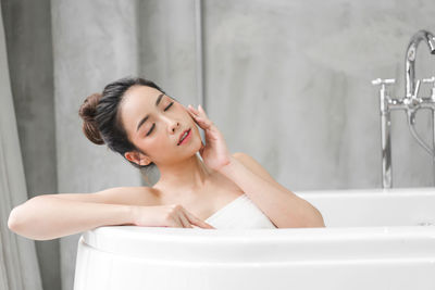 Young woman looking away while sitting in bathroom