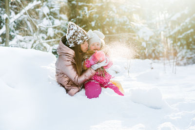 Cheerful mother with daughter playing on snow covered land during winter