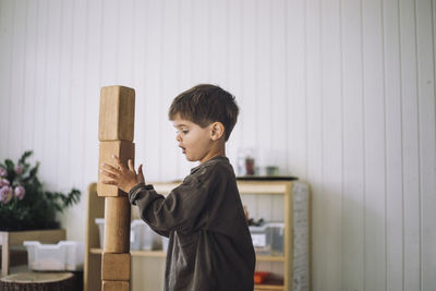 Side view of boy stacking toy blocks while playing in classroom at kindergarten