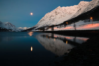 Scenic view of lake by snowcapped mountains against sky at dusk