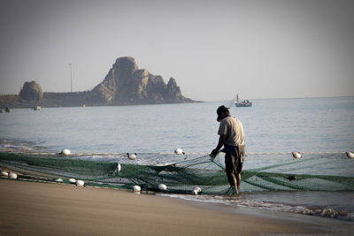 Rear view of fisherman holding fishing net on shore at beach