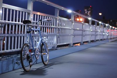 Bicycle parked by railing on footpath at night