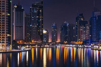 Illuminated buildings by river against sky at night