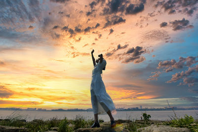 Woman standing by sea against sky during sunset