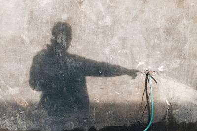 Shadow of man gesturing at garden hose on wall