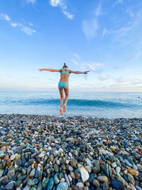 Full length of young woman on pebbles at beach against sky