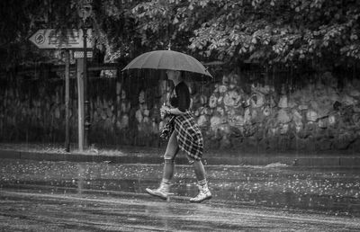 Full length of woman standing on wet umbrella during rainy season