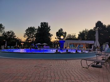 Chairs by swimming pool against sky at dusk