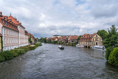 View of buildings by river against cloudy sky