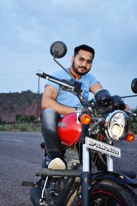 Young man riding motorcycle on road against sky