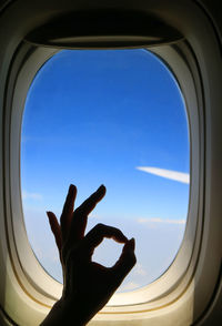 Cropped image of hand gesturing against sky seen through airplane window