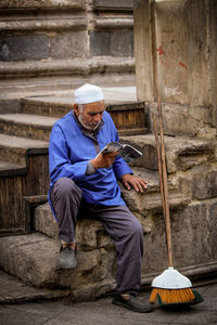 Senior man reading book while sitting on steps by broom