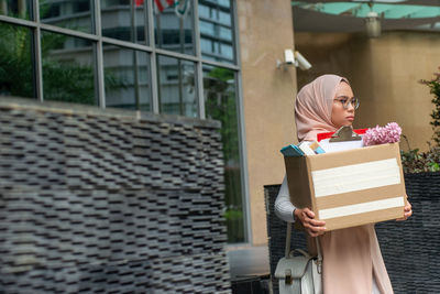 Woman holding umbrella while standing in box