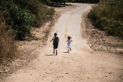 Rear view of people walking on dirt road