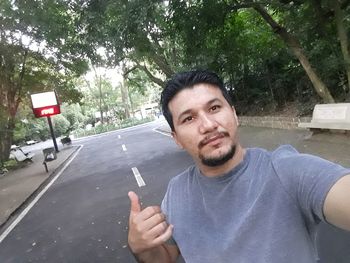 Portrait of young man on road against trees