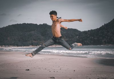 Full length of shirtless man jumping on beach