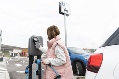 Woman scanning through smart phone at charging station