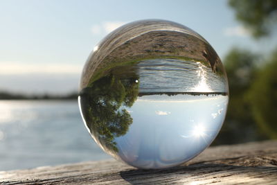 Close-up of crystal ball on wooden post against sky
