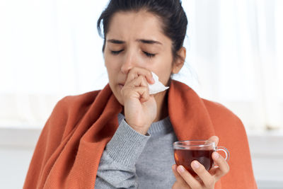 Sick woman wiping nose while holding tea