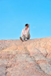 A person sitting on a rock with a bright blue sky