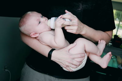 Midsection of father feeding milk while carrying baby at home