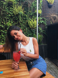 Young woman holding drink while sitting on table