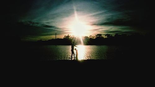 Silhouette people standing on shore against sky during sunset