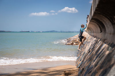 Boy on pier by sea against sky