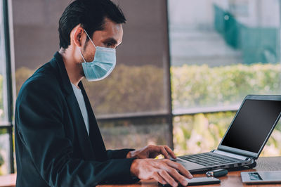 Man wearing mask using laptop at table