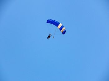 Low angle view of people paragliding against clear blue sky