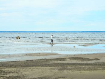 Mid distance view of young man standing at beach against sky