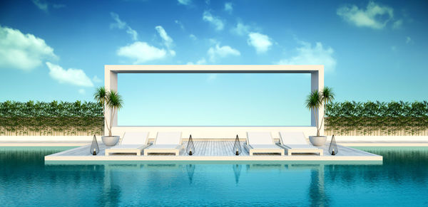 Empty lounge chairs by swimming pool against sky