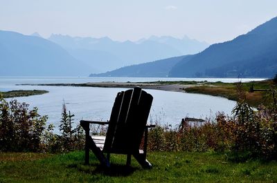 Chair on bench by lake against sky