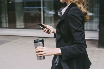 Midsection of businesswoman with coffee mug and phone in city