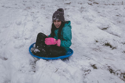 Full length of girl sitting on bobsled in snow