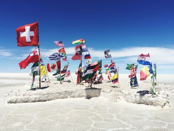 Various flags on beach against blue sky